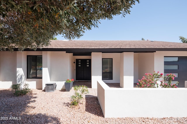 view of front facade with stucco siding, central AC unit, and covered porch