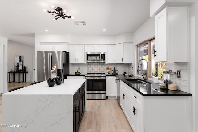 kitchen with stainless steel appliances, a sink, light wood finished floors, recessed lighting, and a kitchen island