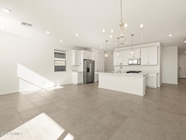 kitchen with light tile patterned floors, appliances with stainless steel finishes, a kitchen island with sink, pendant lighting, and white cabinets