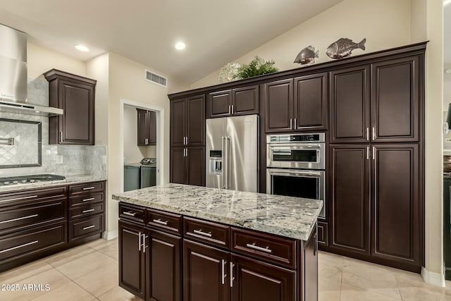 kitchen with vaulted ceiling, stainless steel appliances, washer and clothes dryer, wall chimney range hood, and backsplash