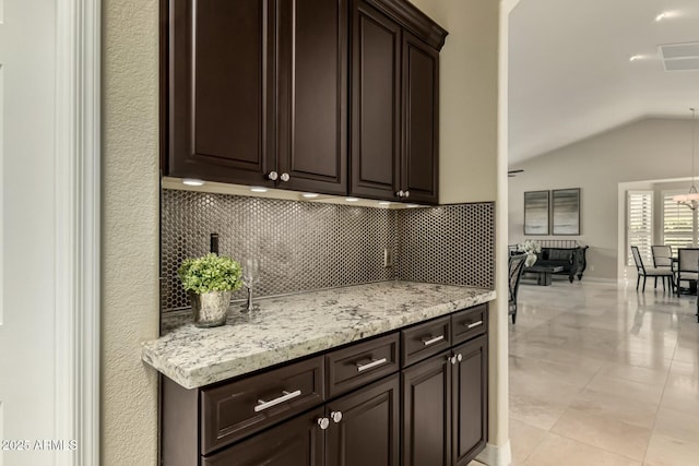 kitchen featuring dark brown cabinets, lofted ceiling, and light stone countertops