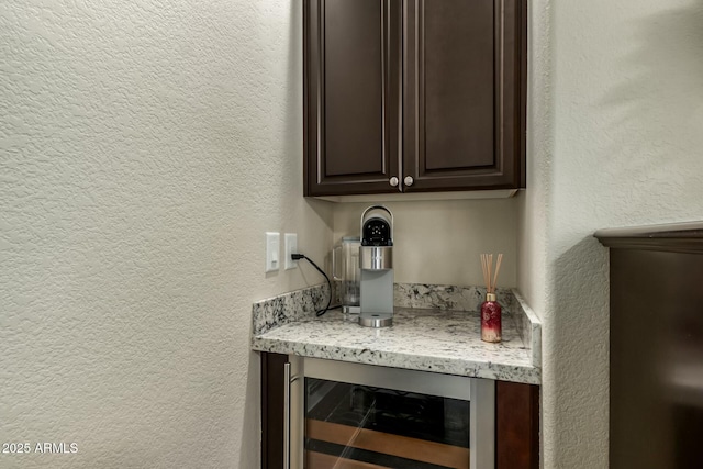 bar with light stone counters, dark brown cabinets, and wine cooler