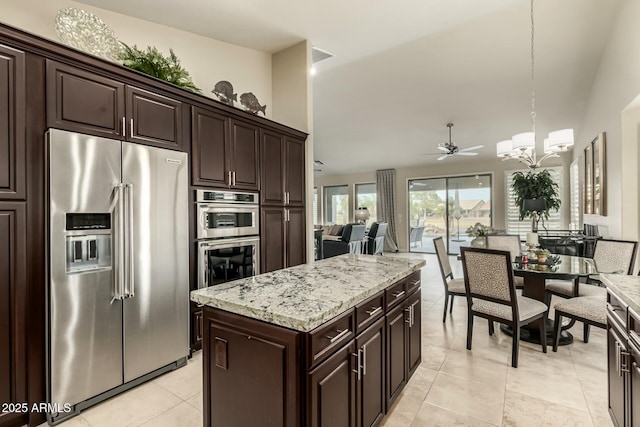 kitchen featuring stainless steel appliances, a center island, dark brown cabinetry, decorative light fixtures, and ceiling fan with notable chandelier