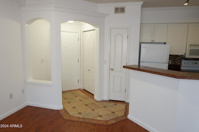 kitchen featuring ornamental molding, backsplash, white appliances, wood-type flooring, and white cabinets