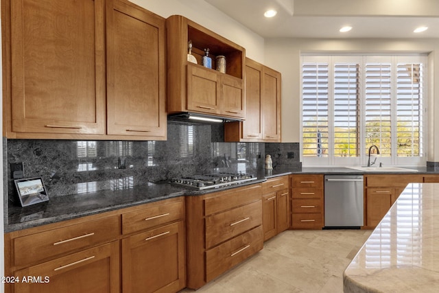 kitchen with tasteful backsplash, stainless steel appliances, light tile patterned floors, sink, and dark stone countertops