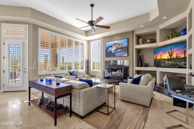 living room with built in features, ceiling fan, a premium fireplace, and a raised ceiling