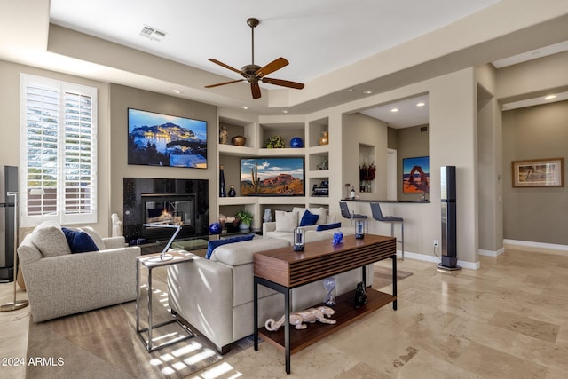 living room with built in shelves, a premium fireplace, and ceiling fan