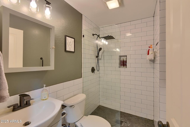 bathroom featuring toilet, tiled shower, a sink, and tile walls