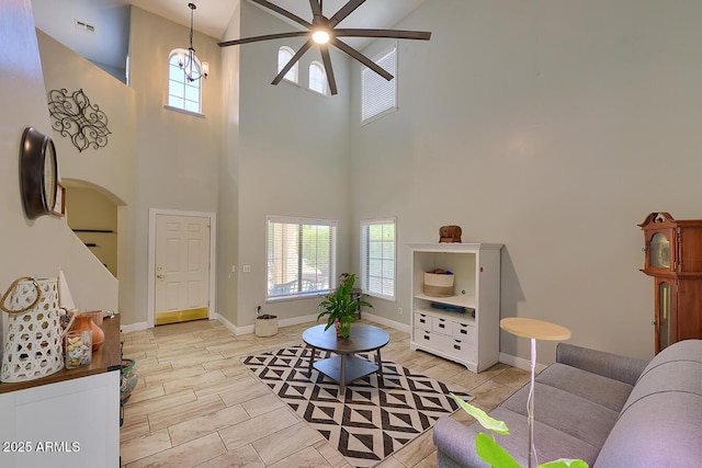 living room with a high ceiling, ceiling fan, arched walkways, baseboards, and visible vents
