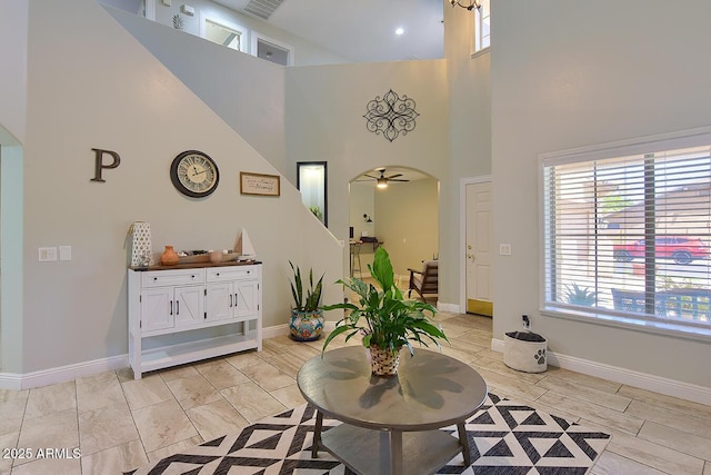 interior space featuring a ceiling fan, stairs, baseboards, a high ceiling, and arched walkways