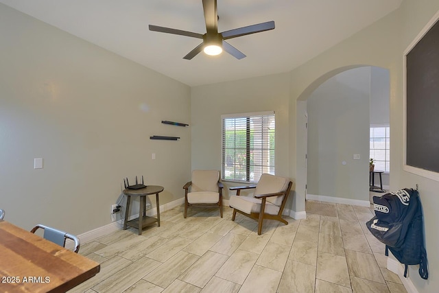 living area featuring arched walkways, ceiling fan, and baseboards
