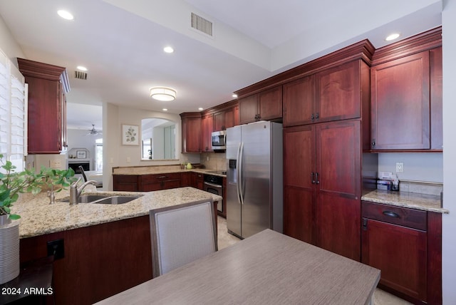 kitchen featuring ceiling fan, sink, light stone counters, kitchen peninsula, and appliances with stainless steel finishes