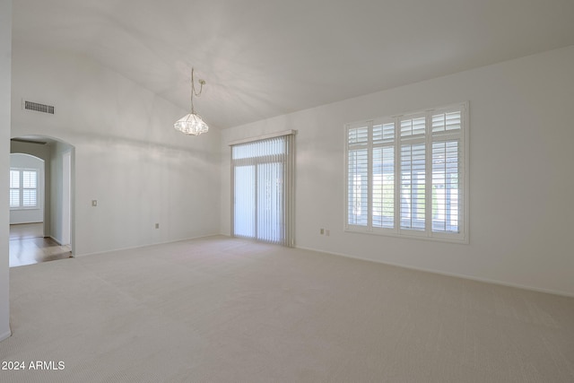 spare room featuring a wealth of natural light, lofted ceiling, light carpet, and a chandelier