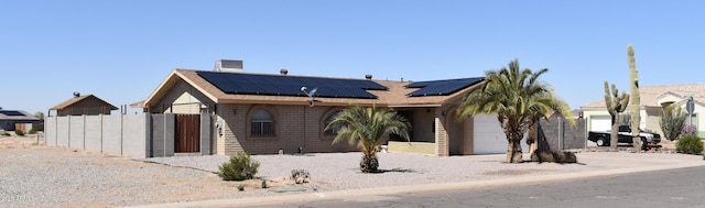 view of front of house with brick siding, roof mounted solar panels, fence, a garage, and driveway