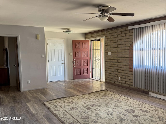 entryway with a ceiling fan, baseboards, brick wall, and wood finished floors