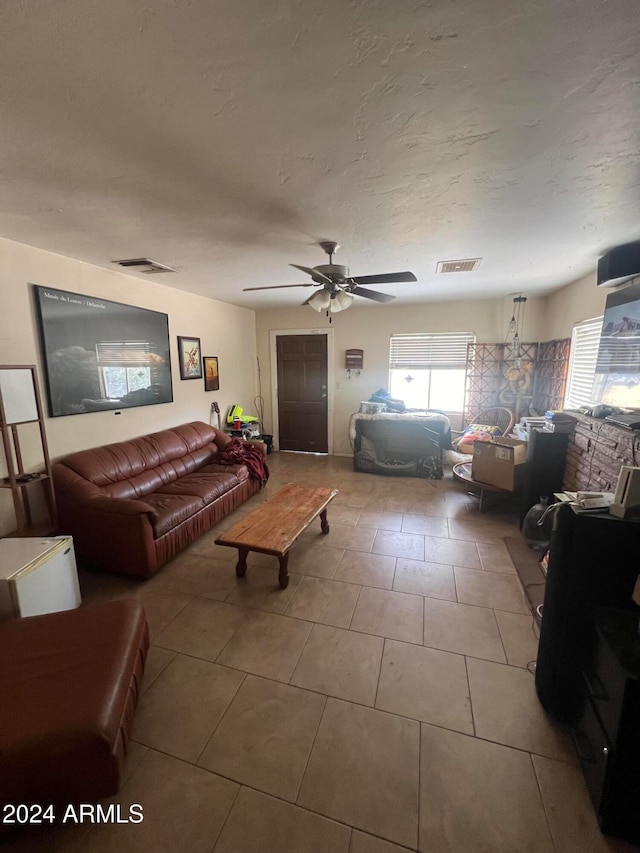 living room featuring a textured ceiling, light tile patterned floors, and ceiling fan