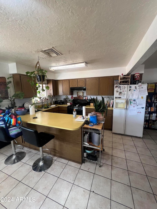 kitchen featuring white fridge with ice dispenser, kitchen peninsula, a textured ceiling, and black range oven