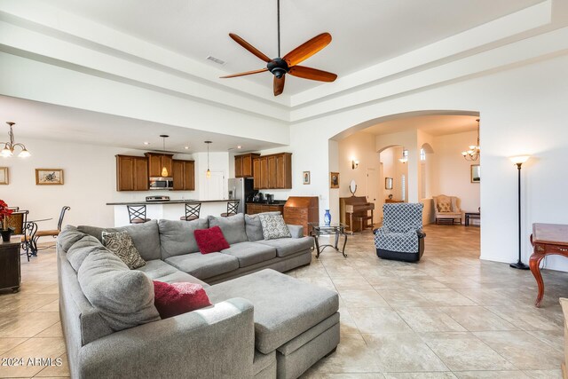 tiled living room with ceiling fan with notable chandelier