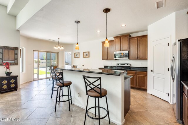 kitchen featuring a kitchen island with sink, stainless steel appliances, decorative light fixtures, an inviting chandelier, and a breakfast bar area