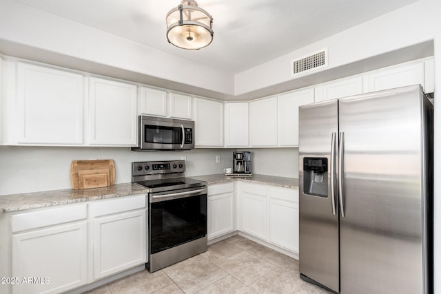 kitchen with white cabinets, light tile patterned floors, stainless steel appliances, and light stone countertops