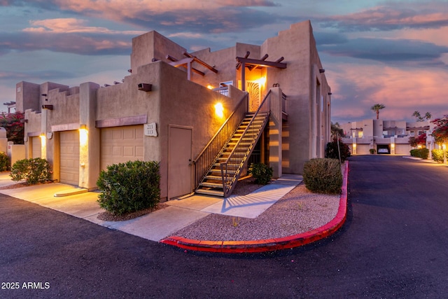 property exterior at dusk featuring a garage, stairs, and stucco siding