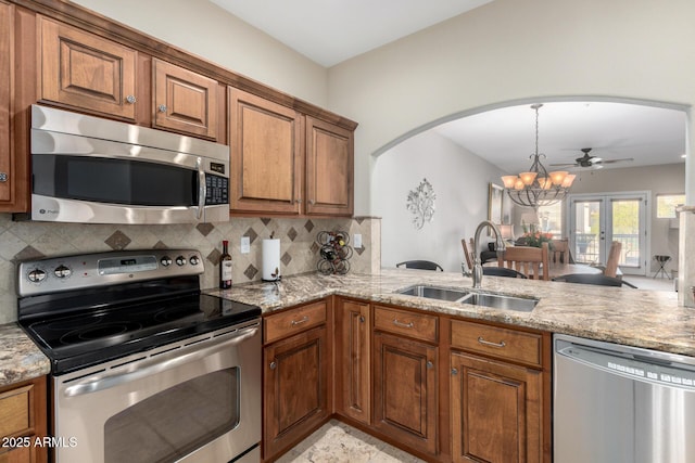 kitchen with decorative backsplash, brown cabinetry, light stone countertops, stainless steel appliances, and a sink