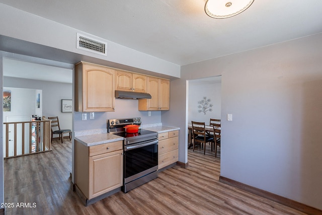 kitchen featuring stainless steel electric range oven, light brown cabinets, under cabinet range hood, dark wood-style flooring, and light countertops