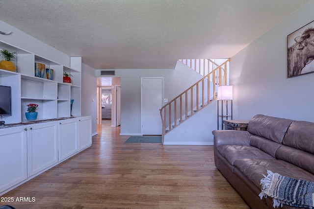 living area featuring wood finished floors, stairs, a textured ceiling, and baseboards