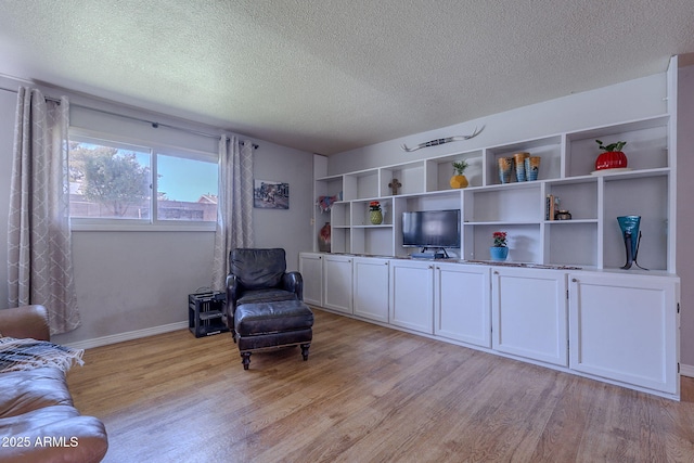 living area with light wood-type flooring, a textured ceiling, and baseboards