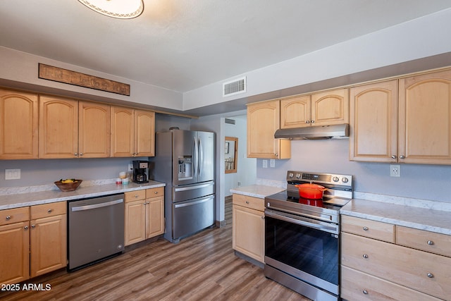 kitchen with stainless steel appliances, under cabinet range hood, light brown cabinets, wood finished floors, and light countertops
