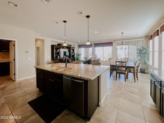 kitchen with light stone counters, sink, decorative light fixtures, dishwasher, and an island with sink