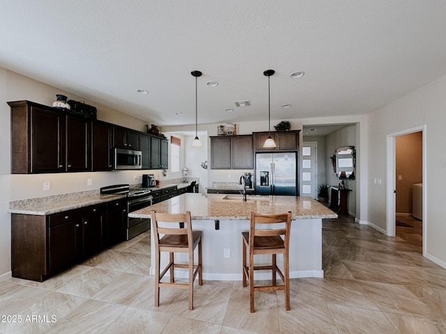 kitchen featuring a breakfast bar, stainless steel appliances, sink, decorative light fixtures, and a center island with sink