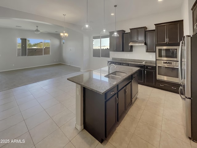 kitchen with stone counters, sink, stainless steel appliances, dark brown cabinets, and a center island with sink