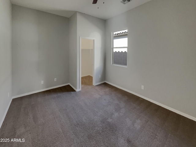 unfurnished bedroom with dark carpet, a walk in closet, a closet, and ceiling fan