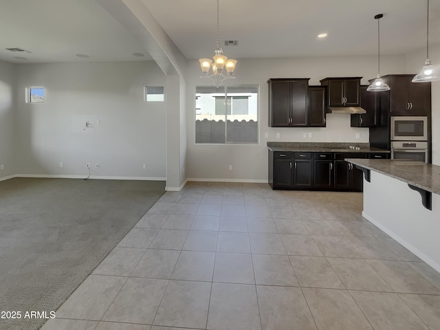 kitchen featuring appliances with stainless steel finishes, hanging light fixtures, dark brown cabinetry, light carpet, and dark stone counters