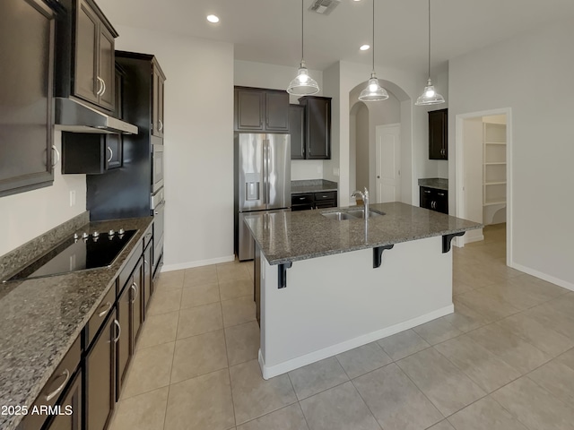 kitchen with sink, dark brown cabinets, stainless steel appliances, a kitchen bar, and dark stone counters