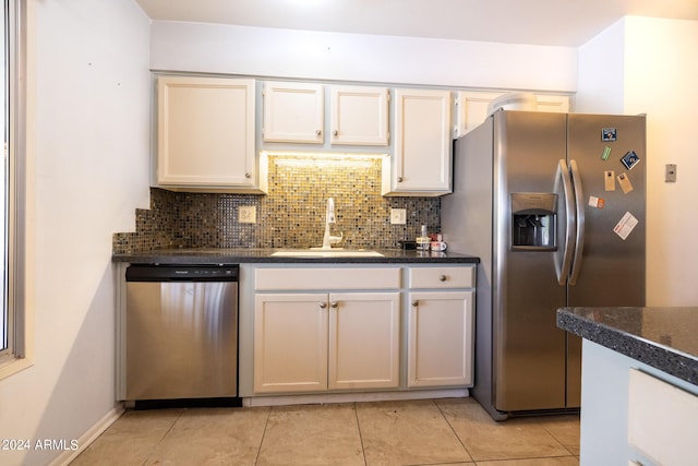 kitchen with light tile patterned floors, decorative backsplash, dark stone counters, appliances with stainless steel finishes, and sink