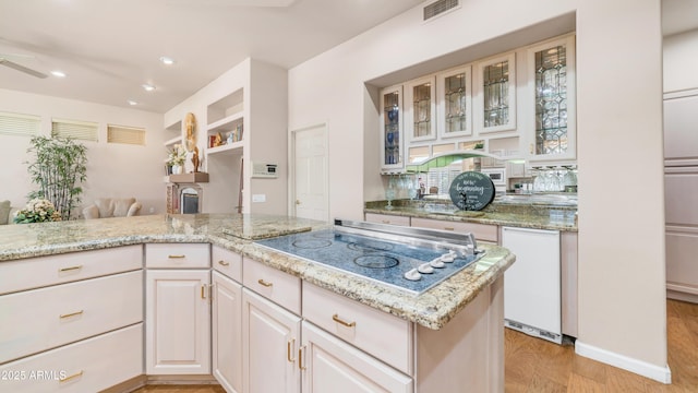 kitchen with light stone counters, glass insert cabinets, black electric stovetop, visible vents, and recessed lighting