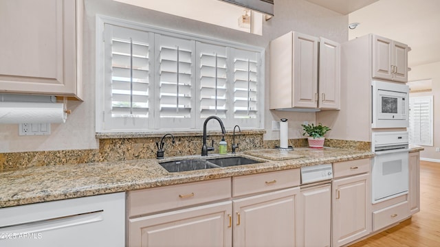 kitchen featuring light stone countertops, a sink, white appliances, and light wood-style floors
