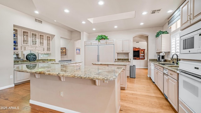 kitchen with arched walkways, visible vents, a skylight, white appliances, and a kitchen island