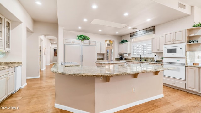 kitchen with arched walkways, light wood-style flooring, a kitchen island, and white appliances