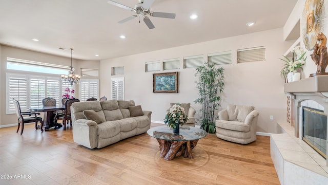 living room featuring a tiled fireplace, recessed lighting, ceiling fan with notable chandelier, and light wood-type flooring
