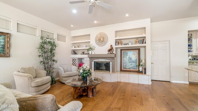 living room with wood finished floors, built in shelves, ceiling fan, a tile fireplace, and baseboards