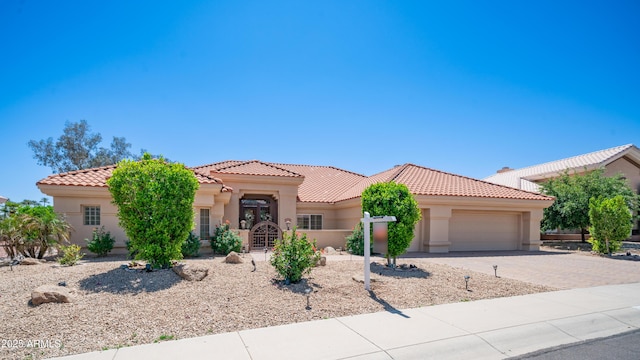 mediterranean / spanish-style home with stucco siding, a tiled roof, driveway, and a garage