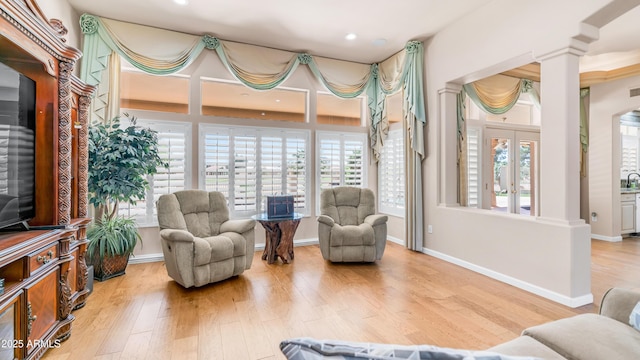 sitting room with baseboards, wood finished floors, ornate columns, and a healthy amount of sunlight