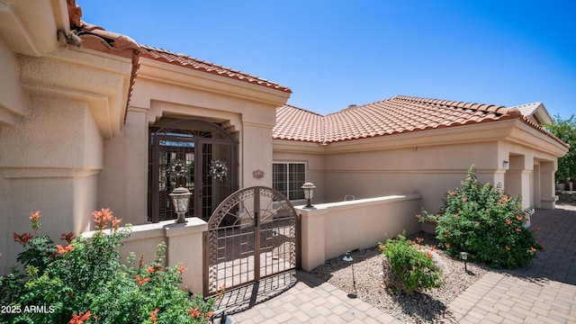 property entrance with a gate, a tile roof, fence, and stucco siding