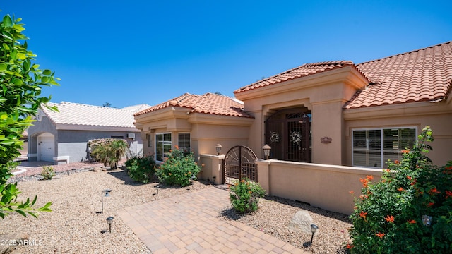 mediterranean / spanish-style home with a gate, a tile roof, a fenced front yard, and stucco siding