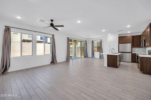 kitchen with a kitchen island with sink, appliances with stainless steel finishes, light countertops, a sink, and open floor plan