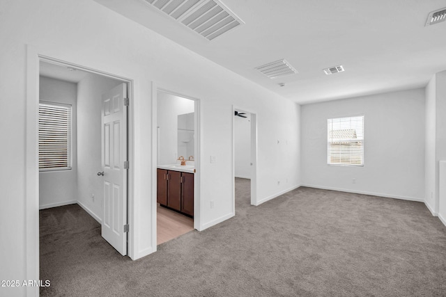 unfurnished bedroom featuring a sink, carpet floors, a walk in closet, and visible vents