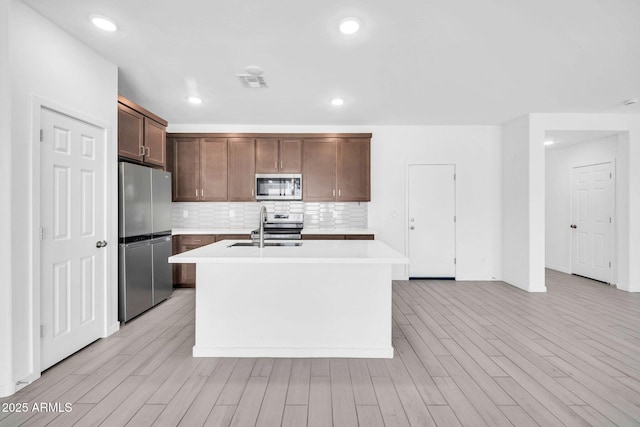 kitchen featuring decorative backsplash, an island with sink, light countertops, a sink, and appliances with stainless steel finishes